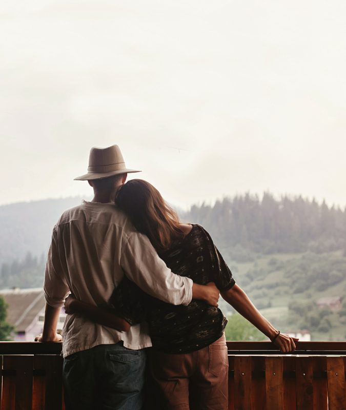 hipster couple hugging on porch of wooden house looking at mount